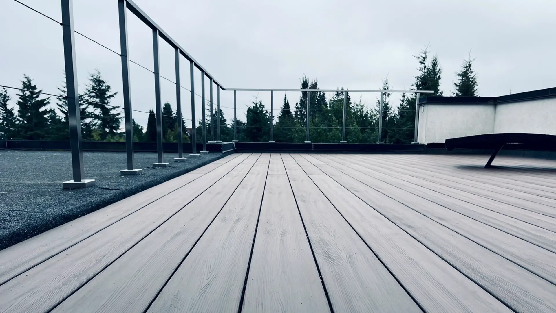 Takterrass i ljusgrå komposittrall med vajerräcke och utsikt mot trädtopparna